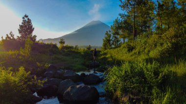 Capture the awe-inspiring view of Semeru Mountain from its foothills, where volcanic ash billows into the sky every minute. Surrounded by vibrant blue skies and diverse trees, clipart