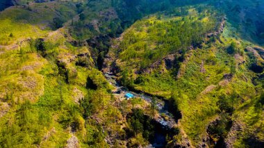 Rinjani Dağı 'nın zirvesine giden yolda yemyeşil ve kahverengi otlardan oluşan bir patika parlak mavi bir gökyüzünün altında uzanıyor. Dinlenme durakları güzergahta nokta.