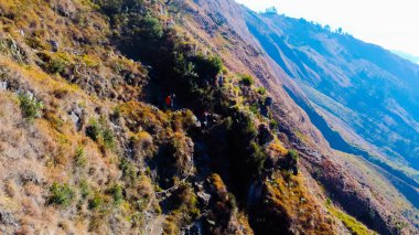 Rinjani Dağı 'nın zirvesine giden yolda yemyeşil ve kahverengi otlardan oluşan bir patika parlak mavi bir gökyüzünün altında uzanıyor. Dinlenme durakları güzergahta nokta.