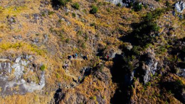 Rinjani Dağı 'nın zirvesine giden yolda yemyeşil ve kahverengi otlardan oluşan bir patika parlak mavi bir gökyüzünün altında uzanıyor. Dinlenme durakları güzergahta nokta.