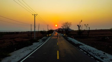 Altın buğday tarlasında dolambaçlı bir yolun manzarası berrak mavi bir gökyüzünün altında, doğanın güzelliğini ve huzurunu somutlaştırıyor..