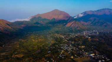 Sembalun 'da, Rinjani Dağı' nın eteklerindeki yuvarlanan tepelerin nefes kesen hava manzarası. Geniş savanalar gün doğumunda altın rengine dönüşüyor..