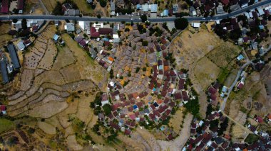 An aerial view of Sade Village in Lombok reveals lush farmland and densely populated homes under the bright midday sun, showcasing vibrant community life. clipart