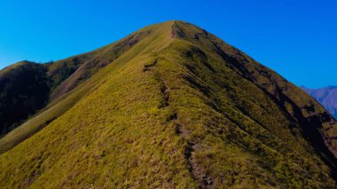 Sembalun 'da, Rinjani Dağı' nın eteklerindeki yuvarlanan tepelerin nefes kesen hava manzarası. Geniş savanalar gün doğumunda altın rengine dönüşüyor..