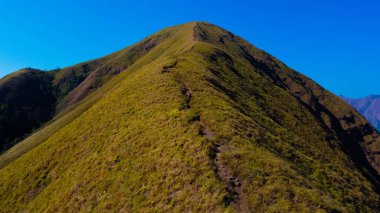 Sembalun 'da, Rinjani Dağı' nın eteklerindeki yuvarlanan tepelerin nefes kesen hava manzarası. Geniş savanalar gün doğumunda altın rengine dönüşüyor..
