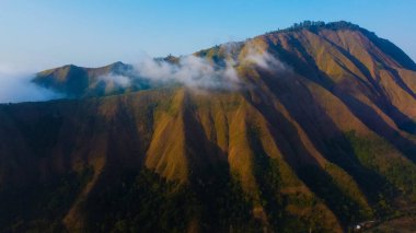 Sembalun 'da, Rinjani Dağı' nın eteklerindeki yuvarlanan tepelerin nefes kesen hava manzarası. Geniş savanalar gün doğumunda altın rengine dönüşüyor..