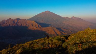 Sembalun 'da, Rinjani Dağı' nın eteklerindeki yuvarlanan tepelerin nefes kesen hava manzarası. Geniş savanalar gün doğumunda altın rengine dönüşüyor..