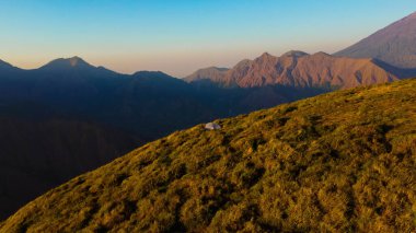 Sembalun 'da, Rinjani Dağı' nın eteklerindeki yuvarlanan tepelerin nefes kesen hava manzarası. Geniş savanalar gün doğumunda altın rengine dönüşüyor..