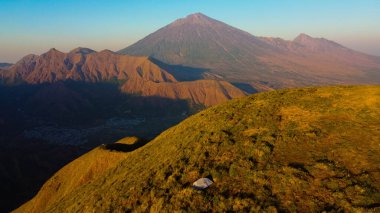 Sembalun 'da, Rinjani Dağı' nın eteklerindeki yuvarlanan tepelerin nefes kesen hava manzarası. Geniş savanalar gün doğumunda altın rengine dönüşüyor..
