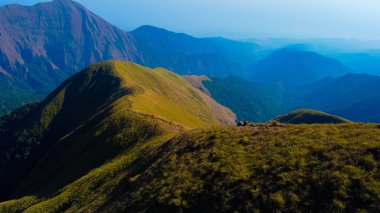 Sembalun 'da, Rinjani Dağı' nın eteklerindeki yuvarlanan tepelerin nefes kesen hava manzarası. Geniş savanalar gün doğumunda altın rengine dönüşüyor..