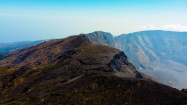 Tambora Dağı 'nın zirvesinin havadan görünüşü mavi gökyüzünün altında nefes kesen bir manzarayı gözler önüne seriyor, güneş doğarken, göz kamaştırıcı arazi üzerinde altın renkler seriyor..
