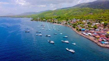 Gün batımında Labuan Bajo limanının hava görüntüsü, çok sayıda pinisi teknesinin kenetlendiğini gösteriyor, büyüleyici yerel konutlar canlı sahneyi çevreledi..