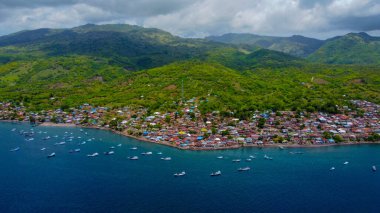 Gün batımında Labuan Bajo limanının hava görüntüsü, çok sayıda pinisi teknesinin kenetlendiğini gösteriyor, büyüleyici yerel konutlar canlı sahneyi çevreledi..
