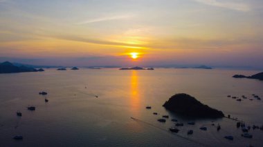 Gün batımında Labuan Bajo limanının hava görüntüsü, çok sayıda pinisi teknesinin kenetlendiğini gösteriyor, büyüleyici yerel konutlar canlı sahneyi çevreledi..