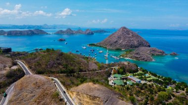 Aerial view of Labuan Bajo harbor at sunset, showcasing numerous pinisi boats docked, with charming local residences surrounding the vibrant scene. clipart