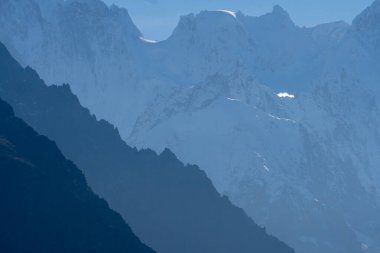 Fransız Alpleri 'nin arka planında beyaz, karlı bir dağa karşı farklı gölgeli dağ sırtları.