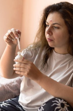 Sivilceye eğilimli genç bir kadının elinde bir serum şişesi ve bir damlatıcıyla yakın plan fotoğrafı. Cilt bakımını, sivilceleri ve yüz bakımını vurgular. Güzellik, cilt bakımı ve kişisel bakım için uygun görsel içerik