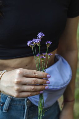 Kadının elinde manikür ve bel çantasıyla küçük bir demet leylak çiçeğini tuttuğu yakın plan.