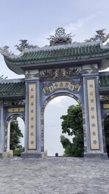 Bu görüntü, kemerinden görülebilen nefes kesici bir kıyı manzarasıyla canlı fayanslar ve sembolik oymalar içeren geleneksel bir Vietnam tapınağı kapısının karmaşık detaylarını yakalar. Linh Ung Zen Manastırı, Da Nang, Vietnam