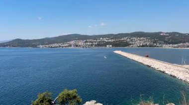 Güzel bir panoramik manzara, Ege Denizi 'nin canlı mavi sularını, uzun bir dalgakıranı ve Yunanistan' ın Kavala kıyı kentini, berrak bir yaz gökyüzünün altında yeşil tepelere yuva yapmış şekilde yakalıyor..