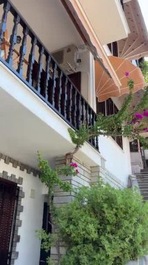 Canlı pembe bougainvillea, tente ve klima ile süslenmiş, güneşli ve davetkar bir atmosferde eski taş merdivenleri yukarı çıkaran bir binanın resimsel görüntüsü..