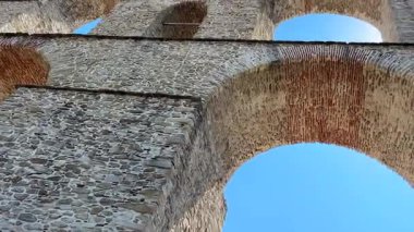 Yunanistan 'ın Kavala kentindeki antik Kamares su kemeri, etkileyici taş kemerlerini parlak mavi bir yaz gökyüzüne karşı sergiliyor. Kalabalık bir şehirde tarihi bir dönüm noktası.