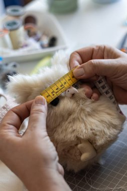 El işçisinin elleri, sarı şeritli şirin, tüylü pelüş bir oyuncağı ölçer, el yapımı doldurulmuş bir hayvan yapar..