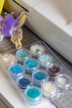 Bir hasırın üzerindeki temiz kaplarda bulunan mavi-beyaz boncuklar. Bir dikiş makinesi & kelebek bu yaratıcı zanaat alanını tanımlar.