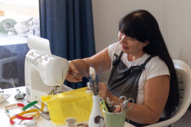 Dikiş makinesindeki kadın, parlak sarı kumaş ustası. Yakınlardaki bant ve makas yaratıcı bir hobi..