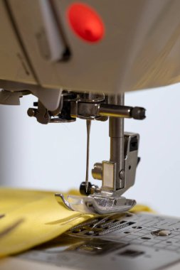 Ayrıntılı yakın plan: Dikiş makinesi iğnesi, basınçlı ayak ve beslenme köpekleri tam olarak sarı kumaşı dikiyorlar, yaratılış sürecinin karmaşıklığını vurguluyorlar..