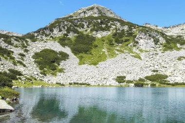 Bulgaristan 'ın Pirin Dağları' nda, engebeli zirveler ve berrak mavi gökyüzünün altındaki yemyeşil dağlarla çevrili buzul gölü nefes kesici bir manzara..