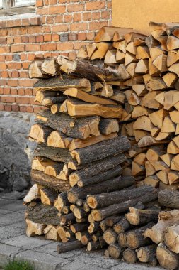 Geniş, düzgün istiflenmiş bir odun yığını çeşitli kütükler ve kırsal parçalar tuğla ve sarı bir duvarın karşısında duruyor. Bu bol erzak soğuk kış aylarında ısıtılmaya hazırdır..