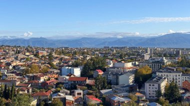 Kutaisi, Georgia: Panoramik şehir görüşü. Kırmızı çatılı evler, modern binalar ve açık gökyüzünün altındaki uzak dağlar. Canlı, tarihi bir şehir..