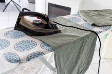 Ütü masasında giysiler. Arka plandaki masanın üzerinde giysiler ütülüyor..