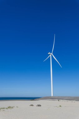 Arka planda mavi gökyüzü olan kum tepelerinde rüzgar türbini
