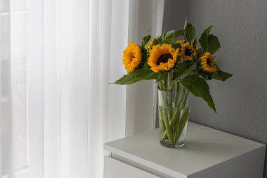 Beyaz bir masadaki cam vazoda ayçiçekleri. Grau arkaplanı 