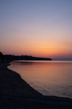 Güzel turuncu-pembe yaz günbatımı Yunan sahillerinde denizin renklerini yansıtıyor.