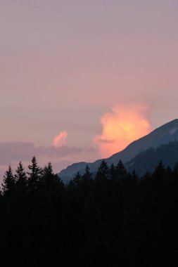 Gün batımında sarı, turuncu ve pembe renkte parlayan bir dağın üstünde bulut.