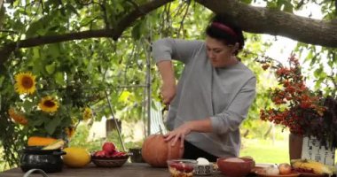 Orta yaşlı kadın Cadılar Bayramı ya da Şükran Günü menüsü için balkabağı hazırlıyor. Büyük balkabağını kesip oymaya çalışıyor. Sonbahar sebzelerinden sağlıklı yemekler pişirmek ve sonbahar hasat süslemeleri yapmak.