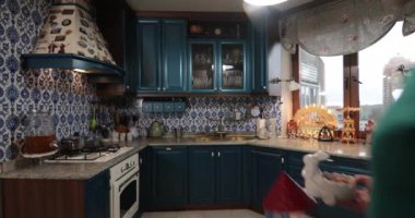Noel kıyafetleri giyen ve kırmızı tayt giyen bir kadın geleneksel mutfaktaki geleneksel sofraya Noel süsleriyle birlikte tabak çanak çömlek koyuyor. Noel yemeği pişirmek için hazırlık. Geniş açı 