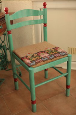 Retro chair makeover into boho style with folk motif embroidered burlap reupholstery of seat. Green painted chair with ethnic upholstery. Renovated furniture with embroidery on seat. Boho interior clipart