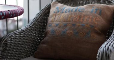Hasır koltukta kırsal yastık. Üzerinde Ukrayna yapımı sarı mavi metin bulunan nakışlı çuval bezi yastığı. El yapımı çapraz dikiş yastıklı Rattan sandalye. Geleneksel nakış. Bulanıklığa doğru odaklan