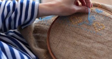 POV kadını eline iğne batırır ve çuval bezi deler. Çapraz dikiş kuş motifini, çuval bezi kumaşında mavi diş ipiyle, ahşap nakış halkasıyla nakışlar. Geleneksel Ukrayna nakış işi mavi sarı renklerde