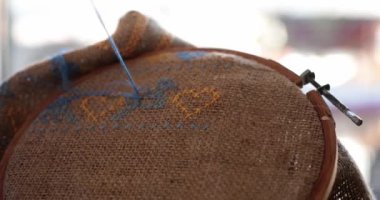 POV el ele tutuşma iğnesi ve nakışlı çapraz dikiş kuş motifi. Çuval bezi kumaşında mavi diş ipi ve ahşap işlemeli halka. Kaba tuval üzerinde mavi sarı renkli geleneksel Ukrayna nakış işi