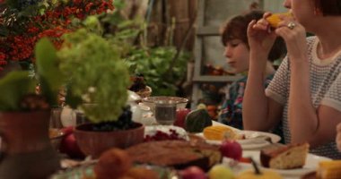 Kadın ısırır ve mısır koçanı yer. 10 yaşındaki çocuk Şükran Günü 'nde yemek masasında oturup, kabak çorbasını çanak çömlekten yiyor. Çocuk ve anne bol bol Şükran Günü sofrasında sağlıklı yiyecekler yiyorlar.