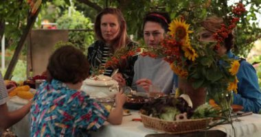 Çeşitli kadınlar ve 10 yaşındaki bir çocuk, sonbahar bahçe partisinde ağacın altındaki kır tarzı masada ev yapımı yemekle Şükran Günü yemeğinin tadını çıkarıyorlar. Arkadaşlar Şükran Günü 'nde birlikte yemek yerler.