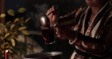 Halk kıyafetleri içinde orta yaşlı bir kadın sıcak sıcak şarabı cam bardaklara dolduruyor. Açık havada Noel pazarında kepçeyle. 40 'lı yaşlardaki kadınlar sıcak bayram içkilerini bardaklara dolduruyor. Geleneksel Noel Gluhwein 'ı