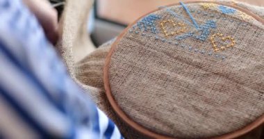 Çizgili elbiseli kişi, elinde iğne, elinde çuval bezi ile çuval bezi, üzerinde mavi diş ipiyle ahşap nakışlı bir halkayla örülmüş kuş motifi taşıyor. Geleneksel Ukrayna nakış işi