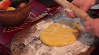 Diz çök ve hamuru yuvarla. Yuvarlak raptiyeyle, kare şeklini alarak, ellerinle bastır. Mutfak tahtası un, yemek takımı, malzemeler masada. Pişirme, pişirme süreci, pasta tarifi.