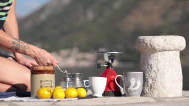 Kadın elleri, Karadağ 'ın Donji Stoliv körfezindeki iskelede piknik yaparken gaz ocağını kapatıyor ve sıcak kahveyi fincana çeviriyor. Kadın kahve yapıp şeker kutusundan şeker ekliyor.
